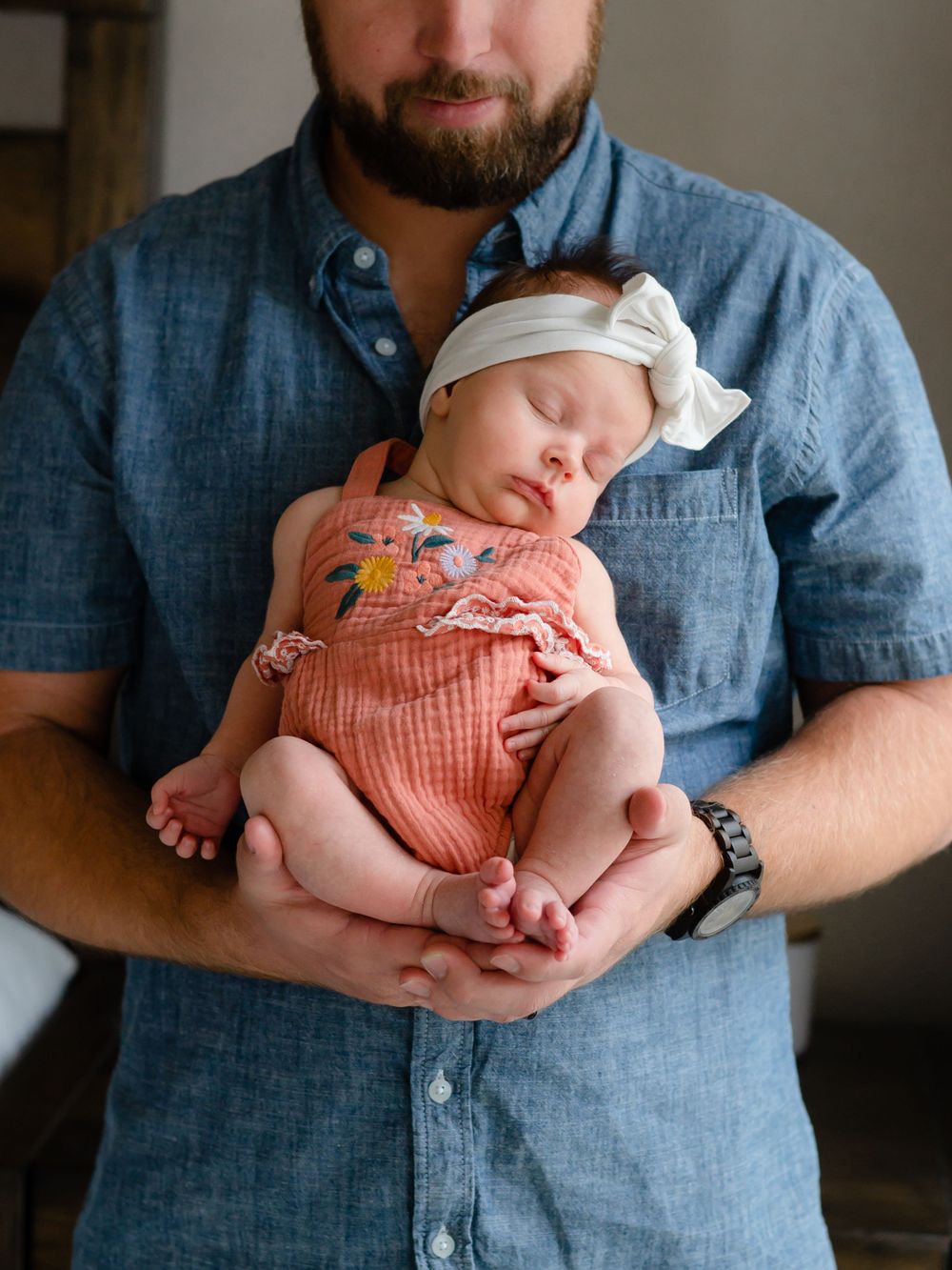Sleeping newborn in pink romper rests peacefully against parent's chest.