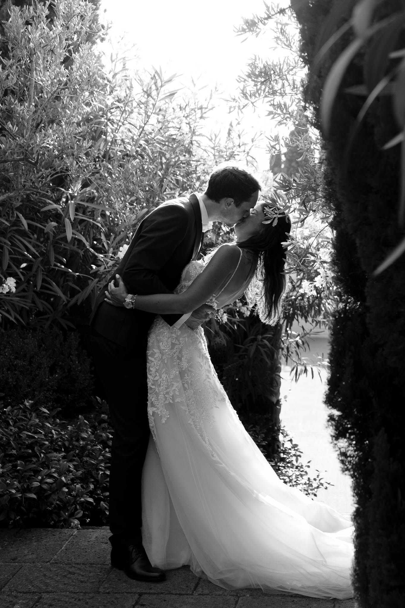 A romantic black and white wedding portrait of a couple sharing a kiss in a lush garden setting.