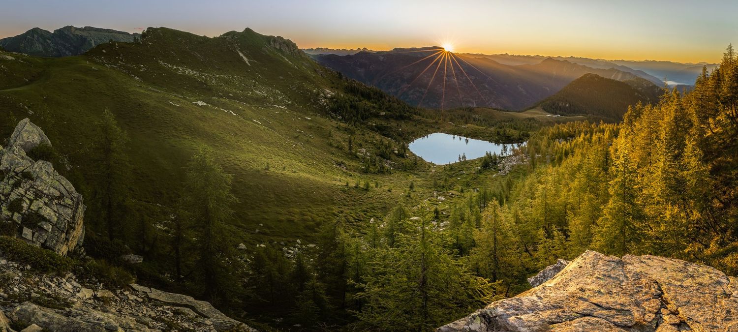 Panoramic view of an alpine lake nestled among mountains with golden larches at sunset.