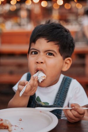 Child in overalls enjoying cake at an outdoor celebration.