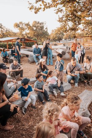 Large group gathered on wooden benches in an outdoor park setting at sunset.