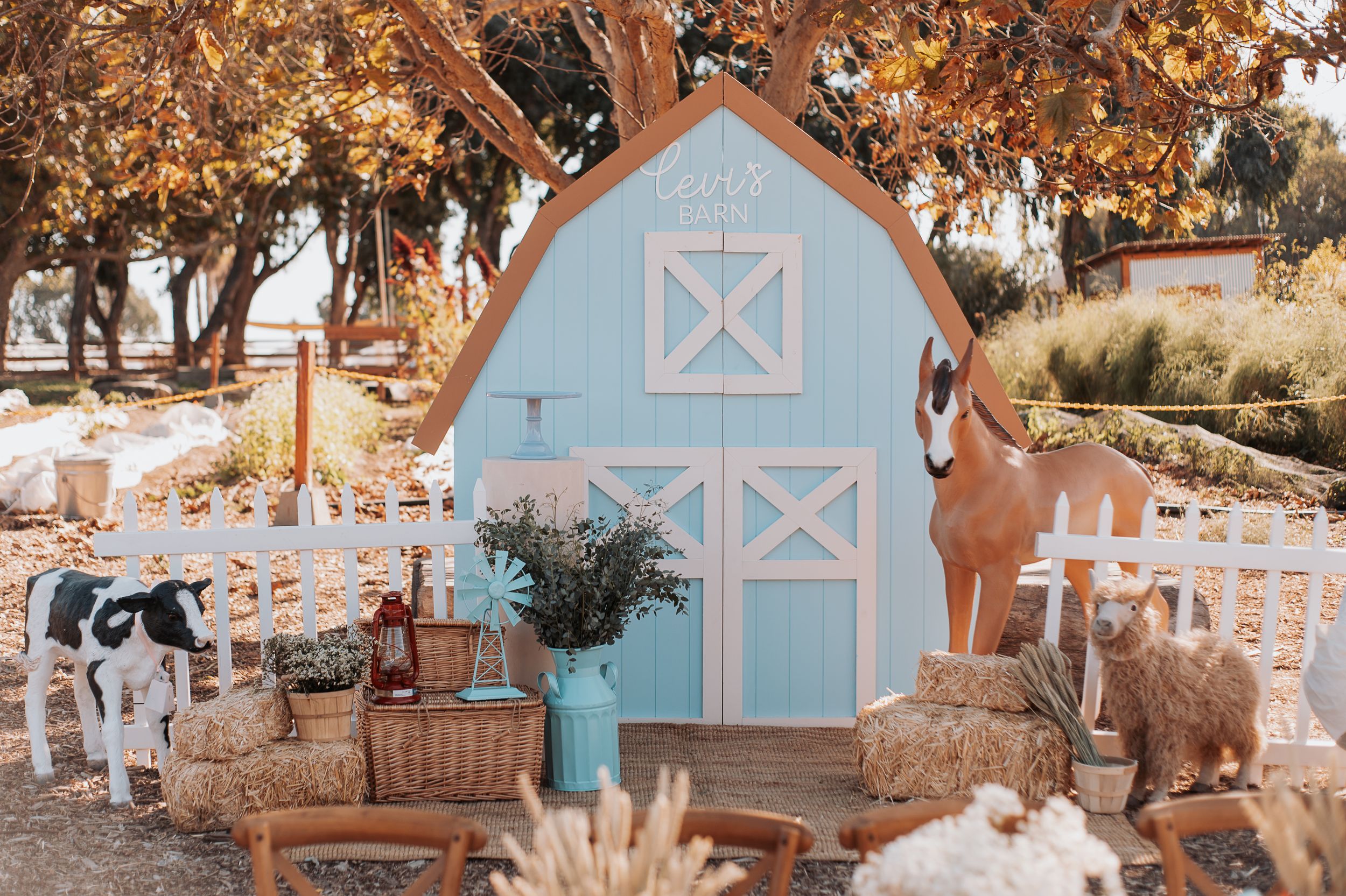 A charming blue barn playhouse decorated with hay bales and white chairs for an outdoor event.