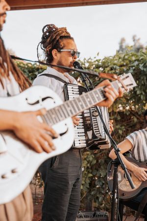 Musicians perform outdoors with an accordion and guitar at a casual outdoor gathering.
