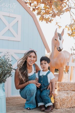 A cheerful scene in front of a light blue barn with autumn trees and decorative horse statue.