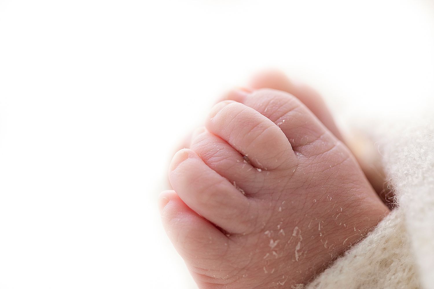 Close-up of tiny newborn's hand with delicate skin folds wrapped in white fabric.