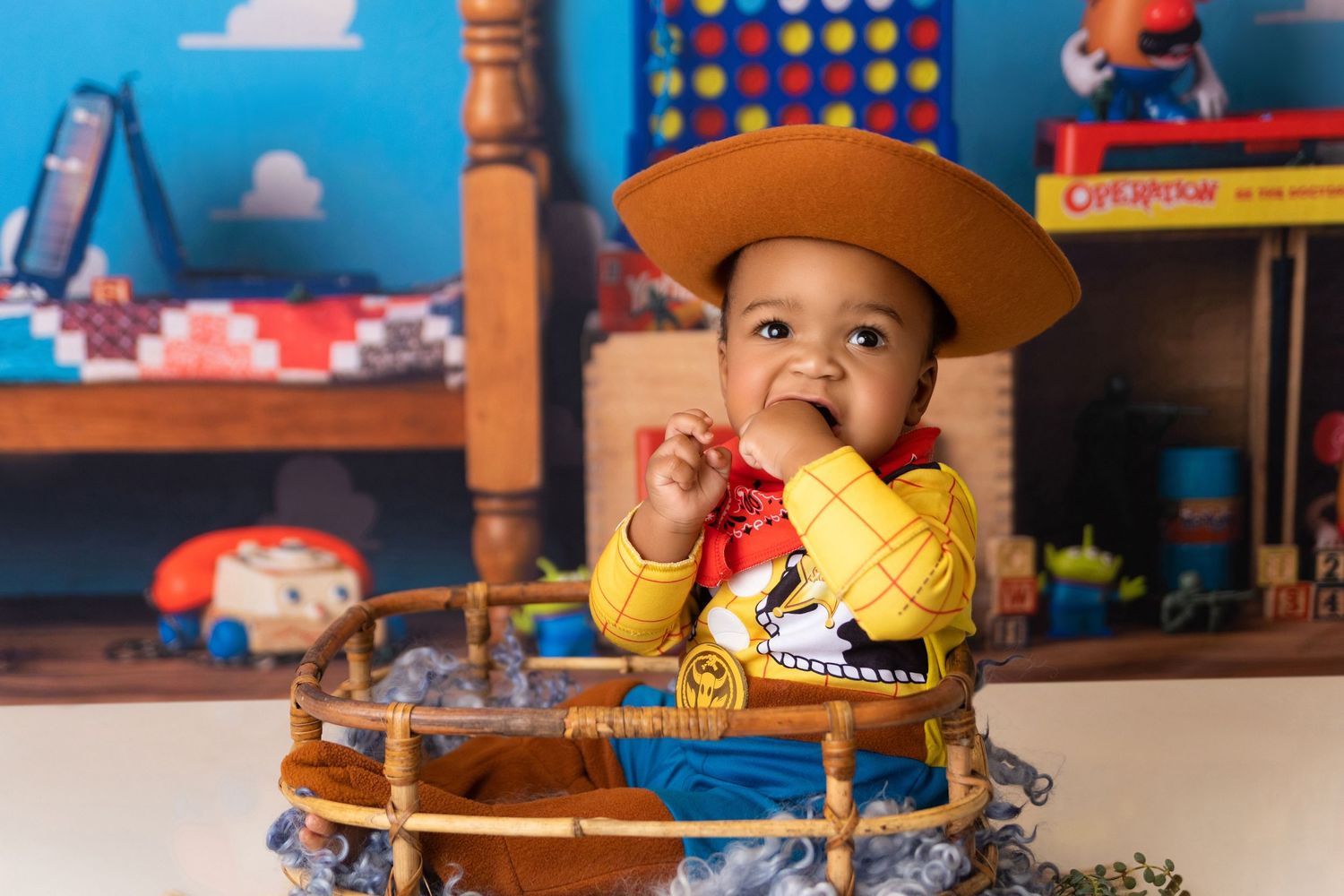 A toddler dressed as Woody from Toy Story sits at a colorful themed celebration.