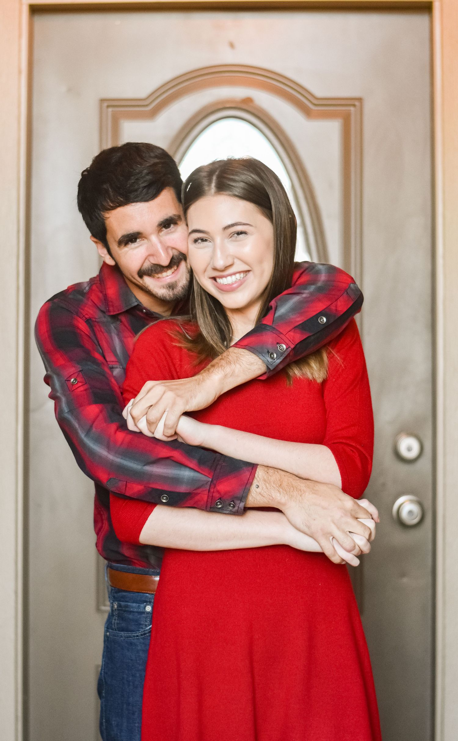 Couple in red embracing and smiling by front door.