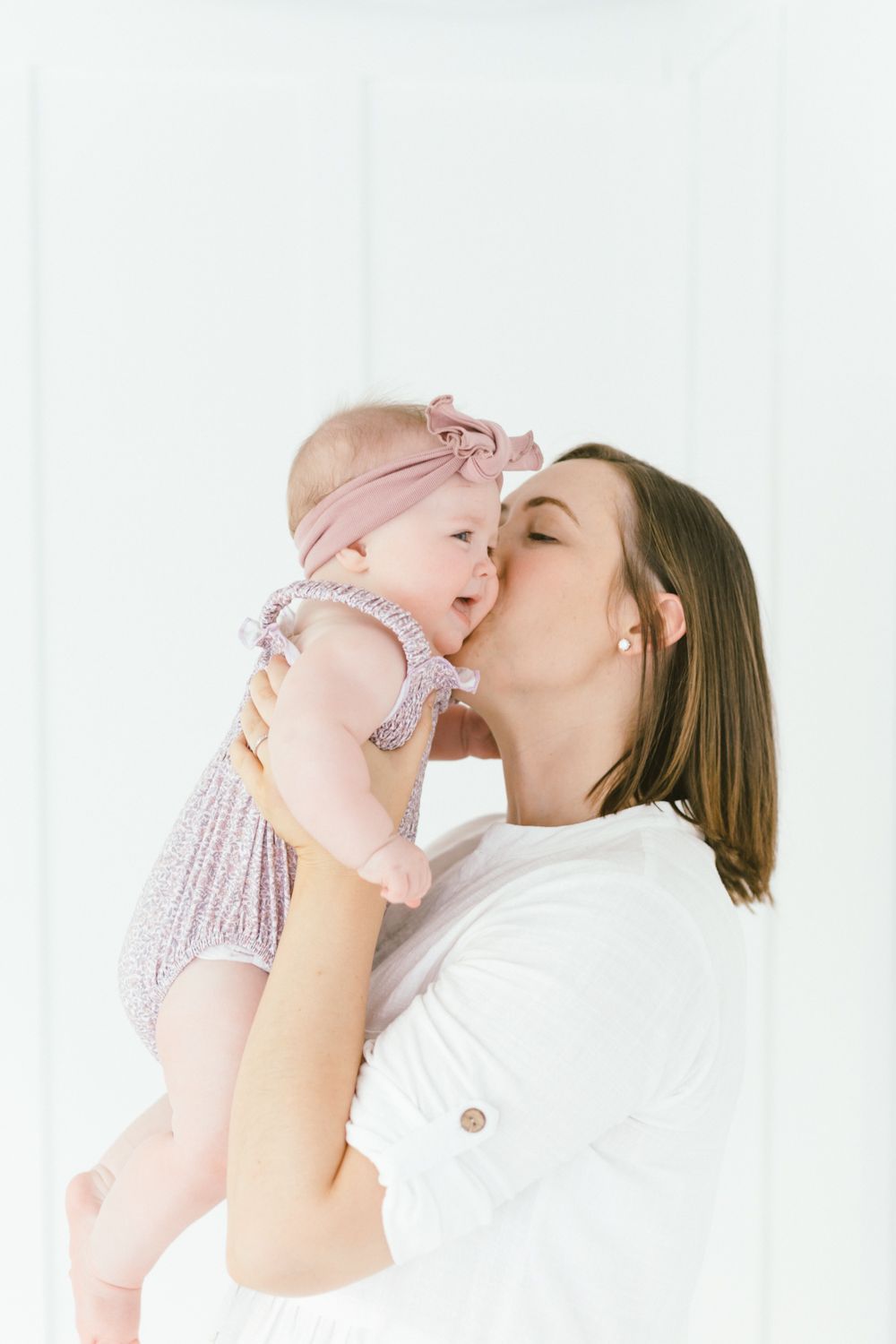 Intimate family moment with baby in pink outfit against white background.