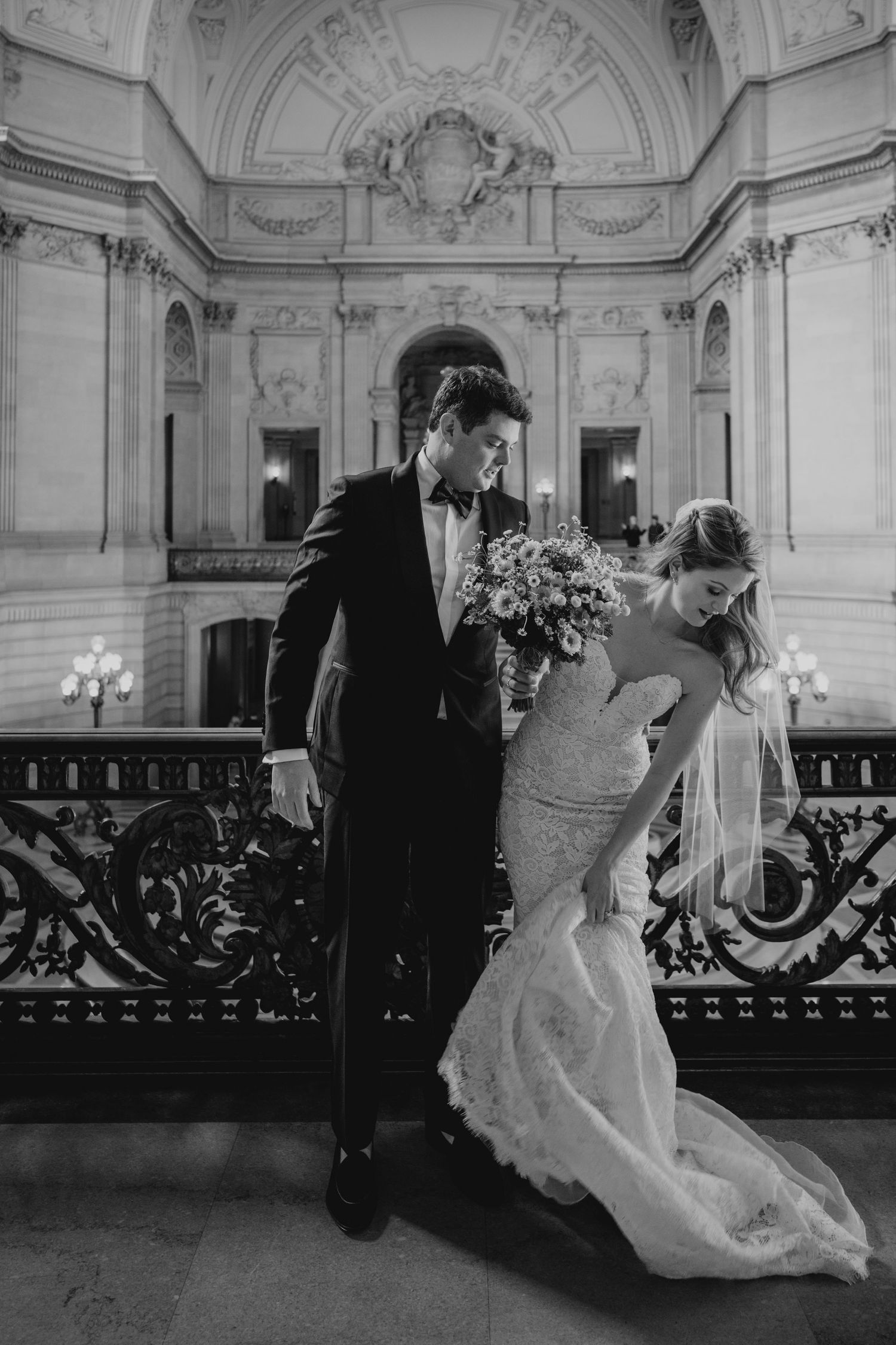 A romantic black and white wedding photo captured in an ornate marble venue with decorative railings.