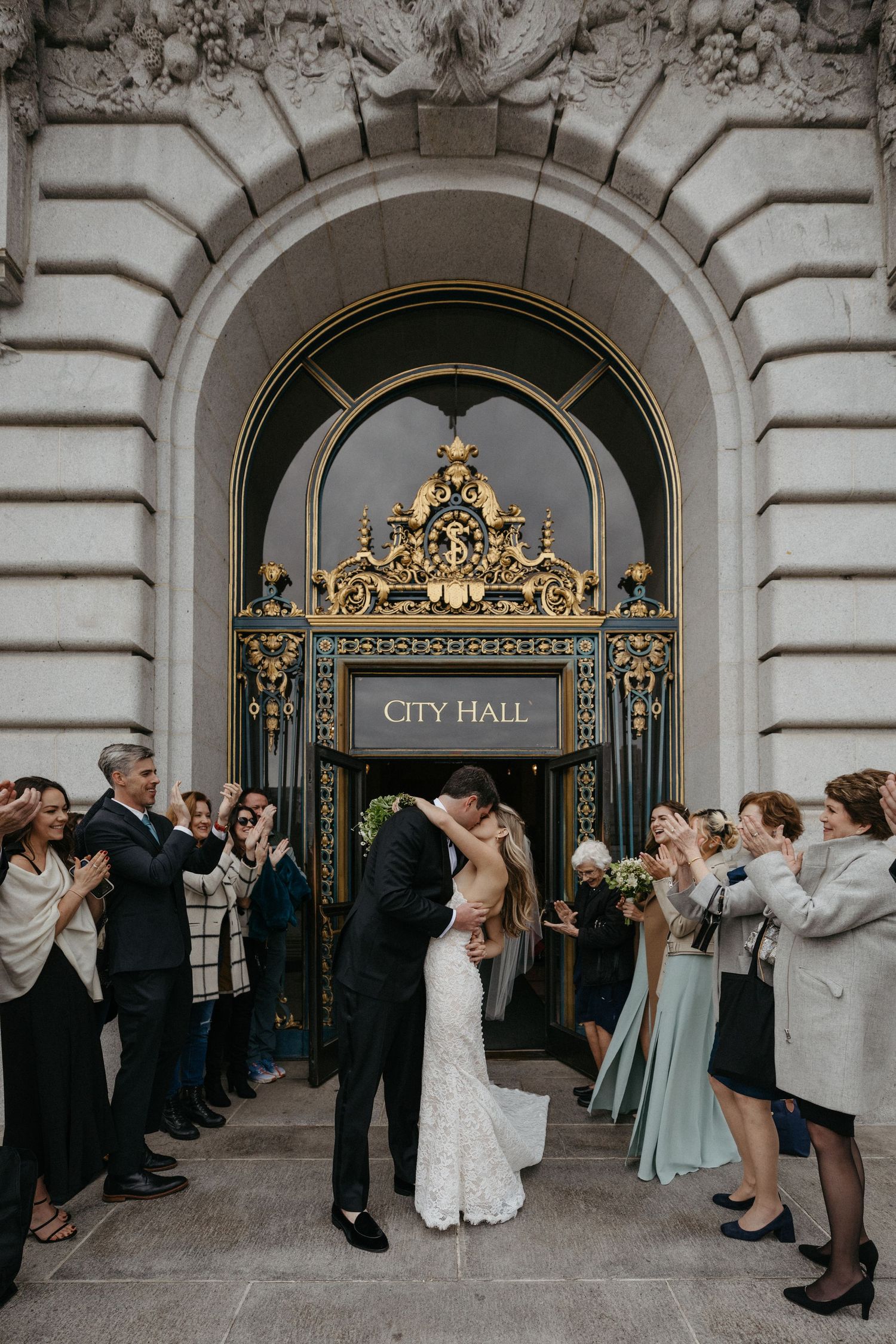 Wedding kiss at City Hall's grand entrance as guests applaud the celebration.