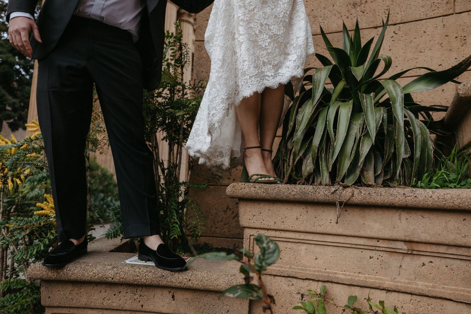 Close-up of formal wedding attire and shoes on stone steps with garden foliage.