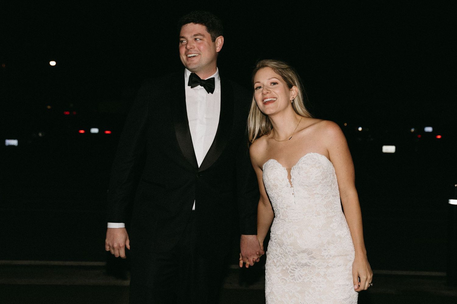 Newlyweds in formal attire share a moment together outdoors at night.