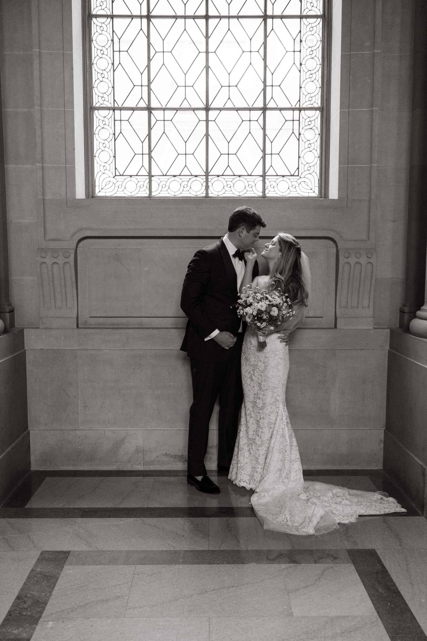 A tender wedding moment captured in black and white beneath an ornate window.