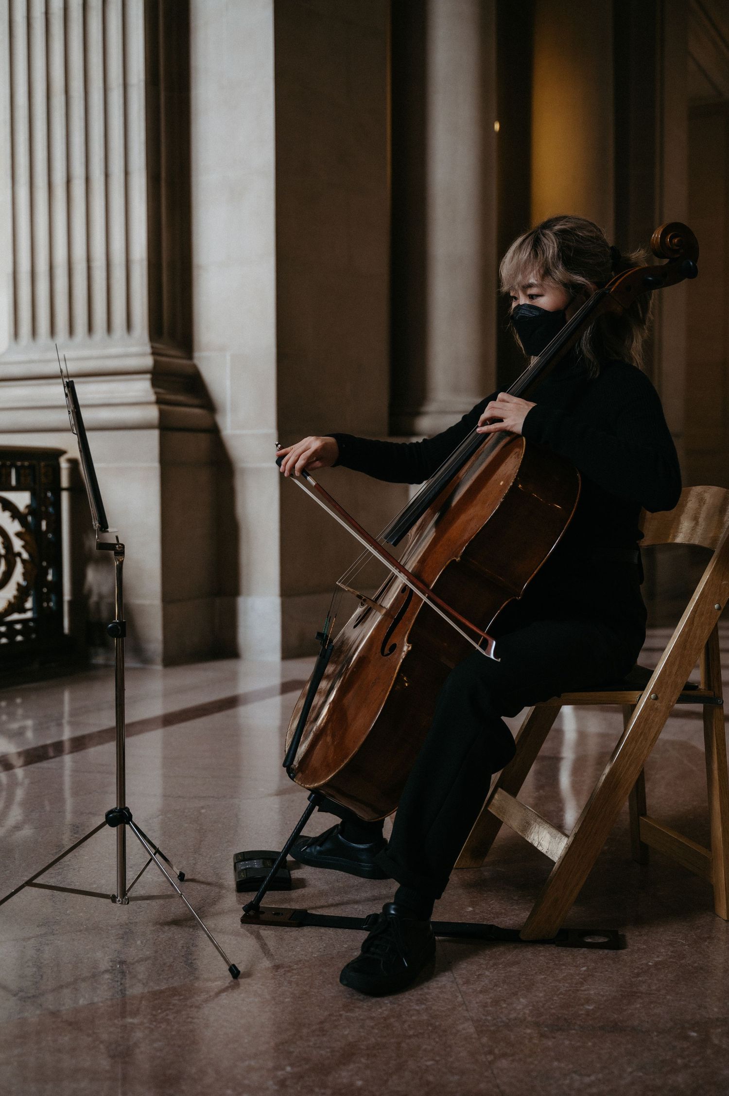 A cellist in black attire performs during a wedding ceremony in an elegant venue.