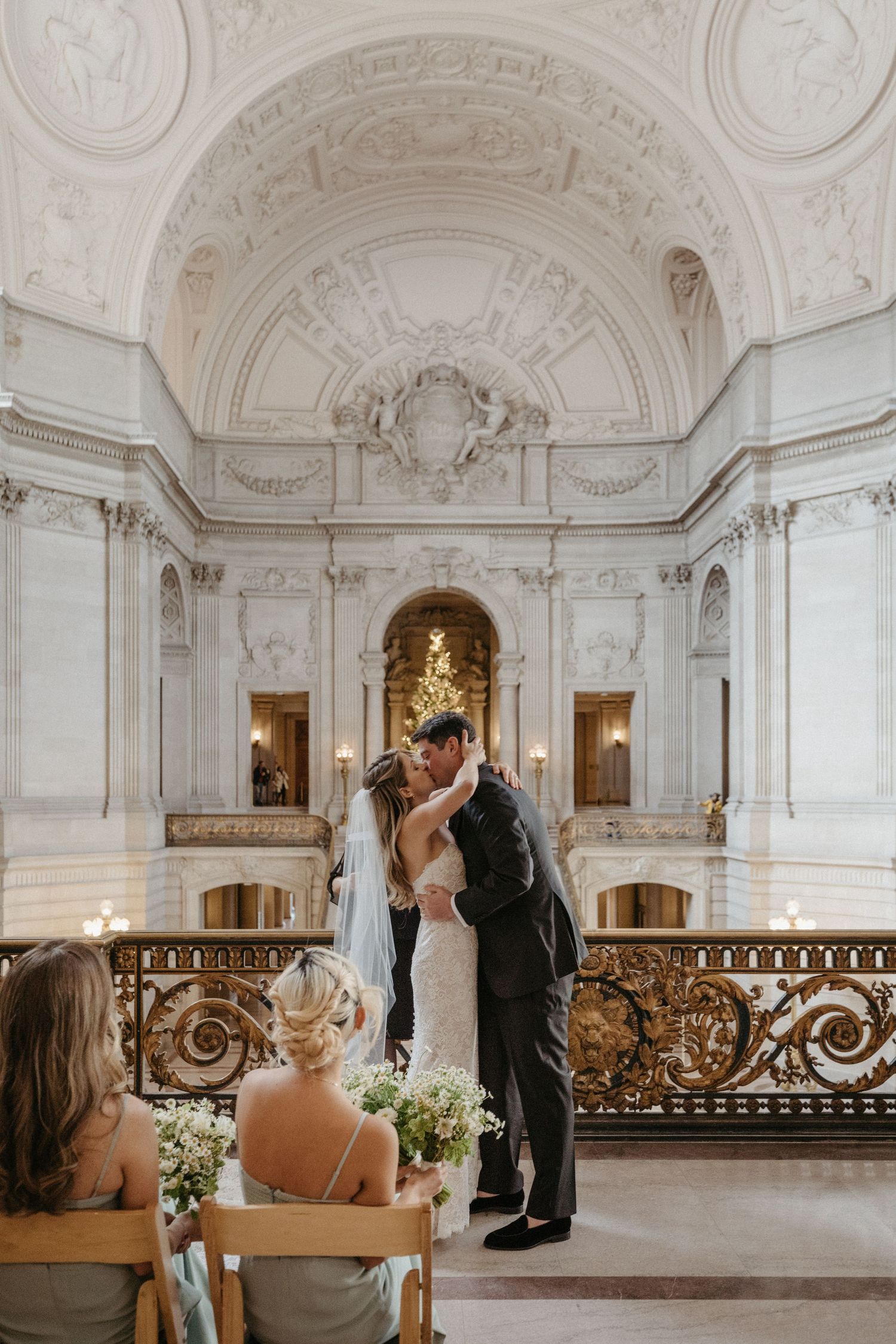 An intimate wedding ceremony in an ornate white marble hall with gilded details.