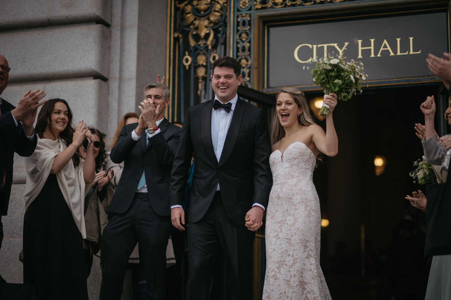 Wedding couple exits City Hall with celebrating guests as newlyweds amid historic architecture.