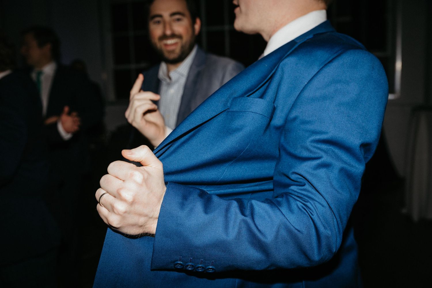 Two wedding guests in suits gesture animatedly during a conversation.