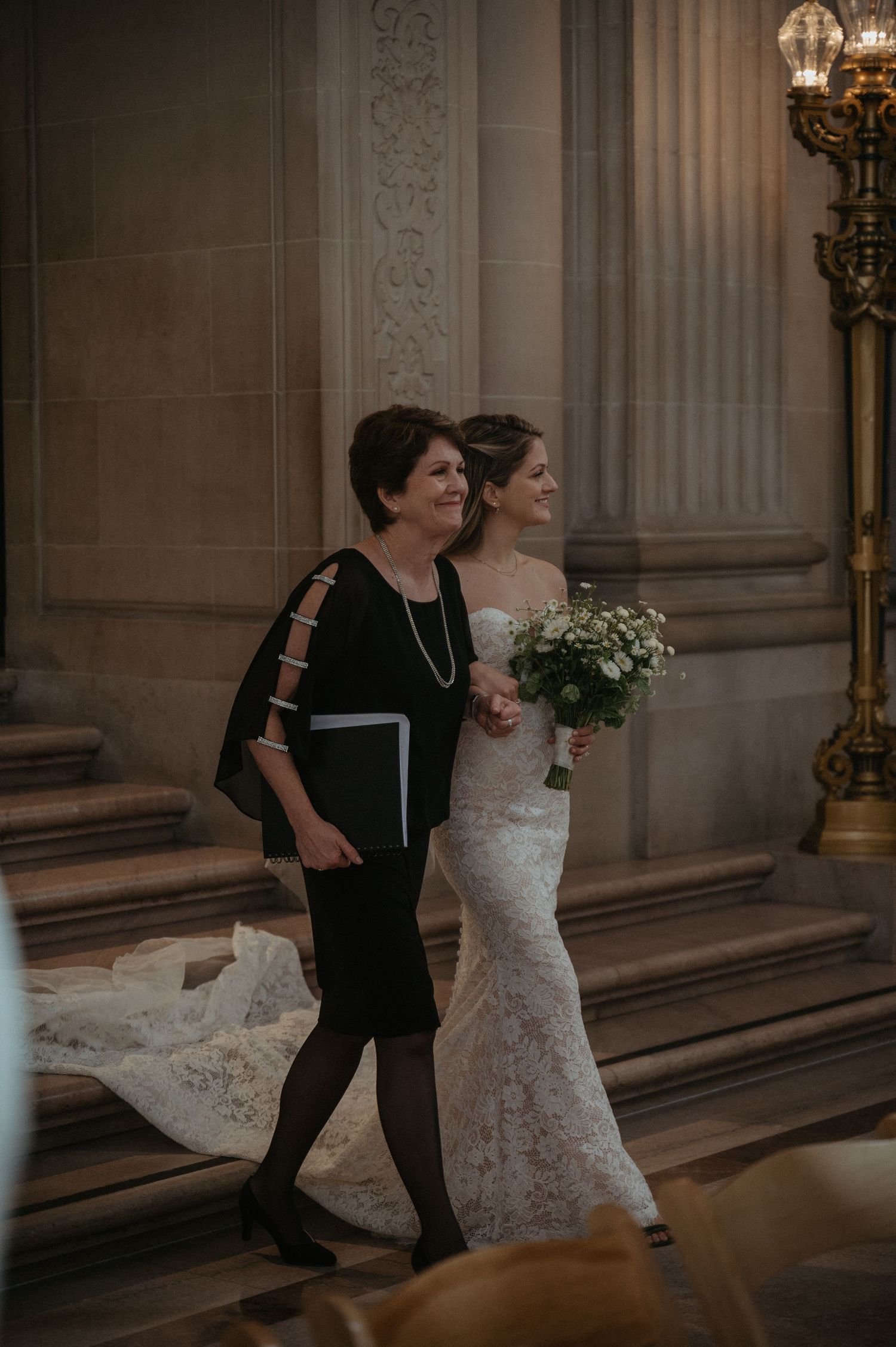 A pair walks together through an elegant venue with classical columns and ornate details.