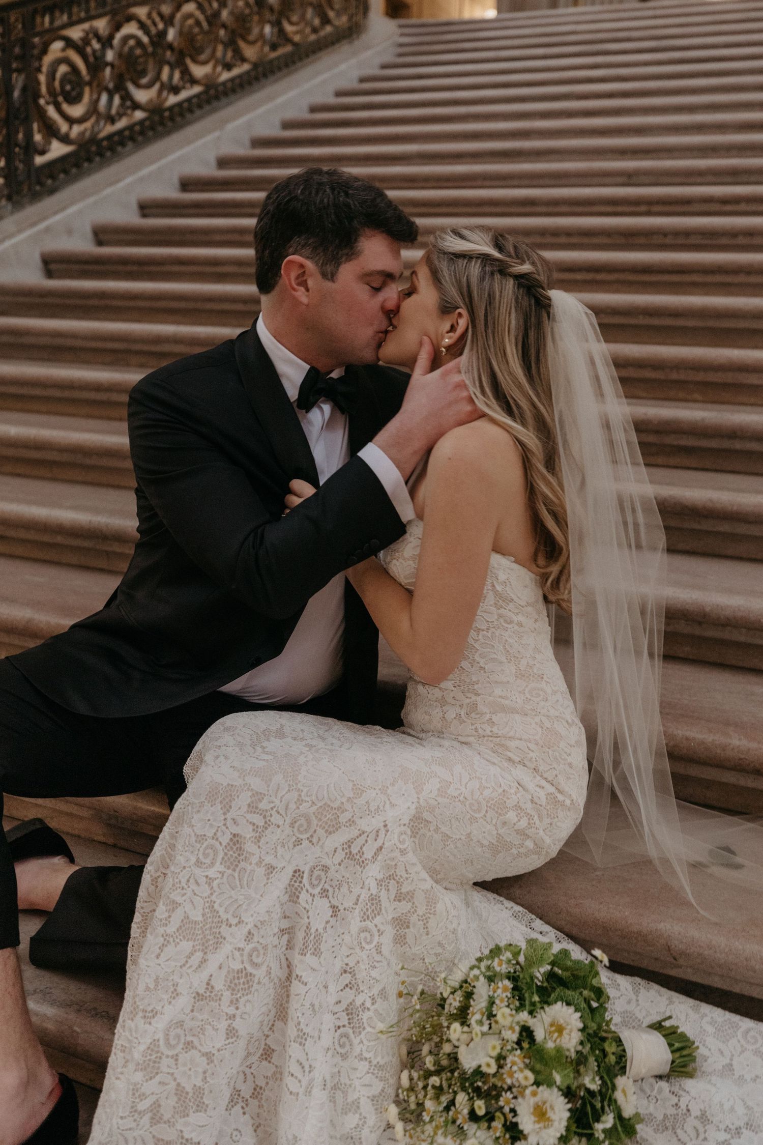 Intimate wedding portrait on ornate staircase with bridal bouquet of white flowers.