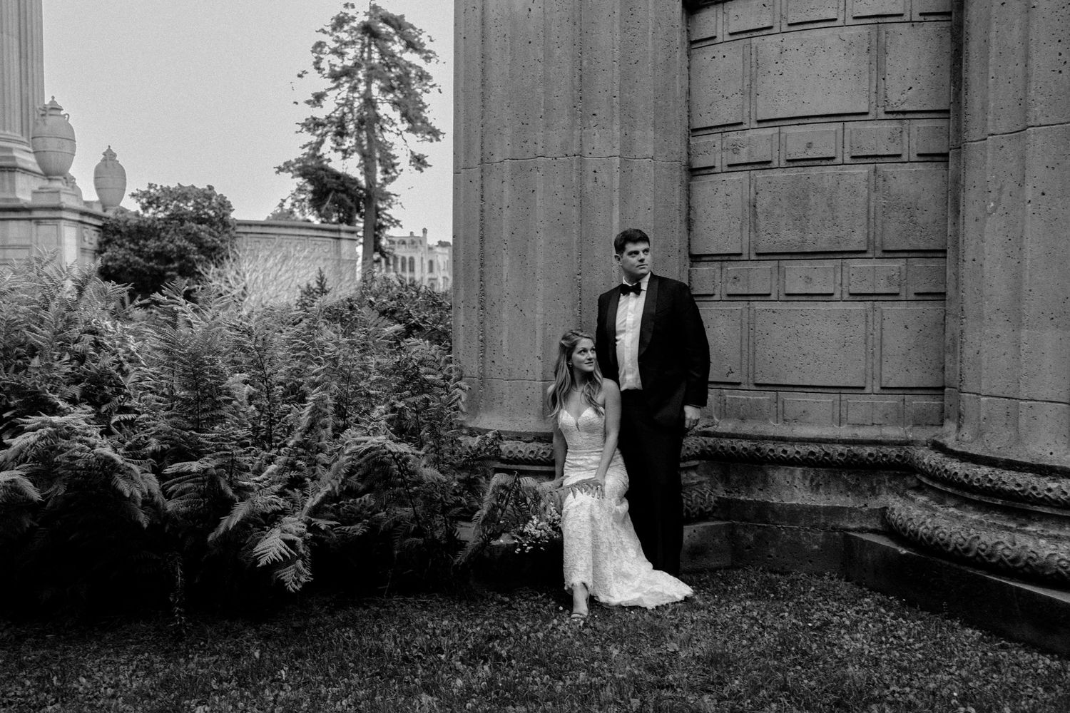 Black and white wedding portrait with couple standing by classical stone columns.
