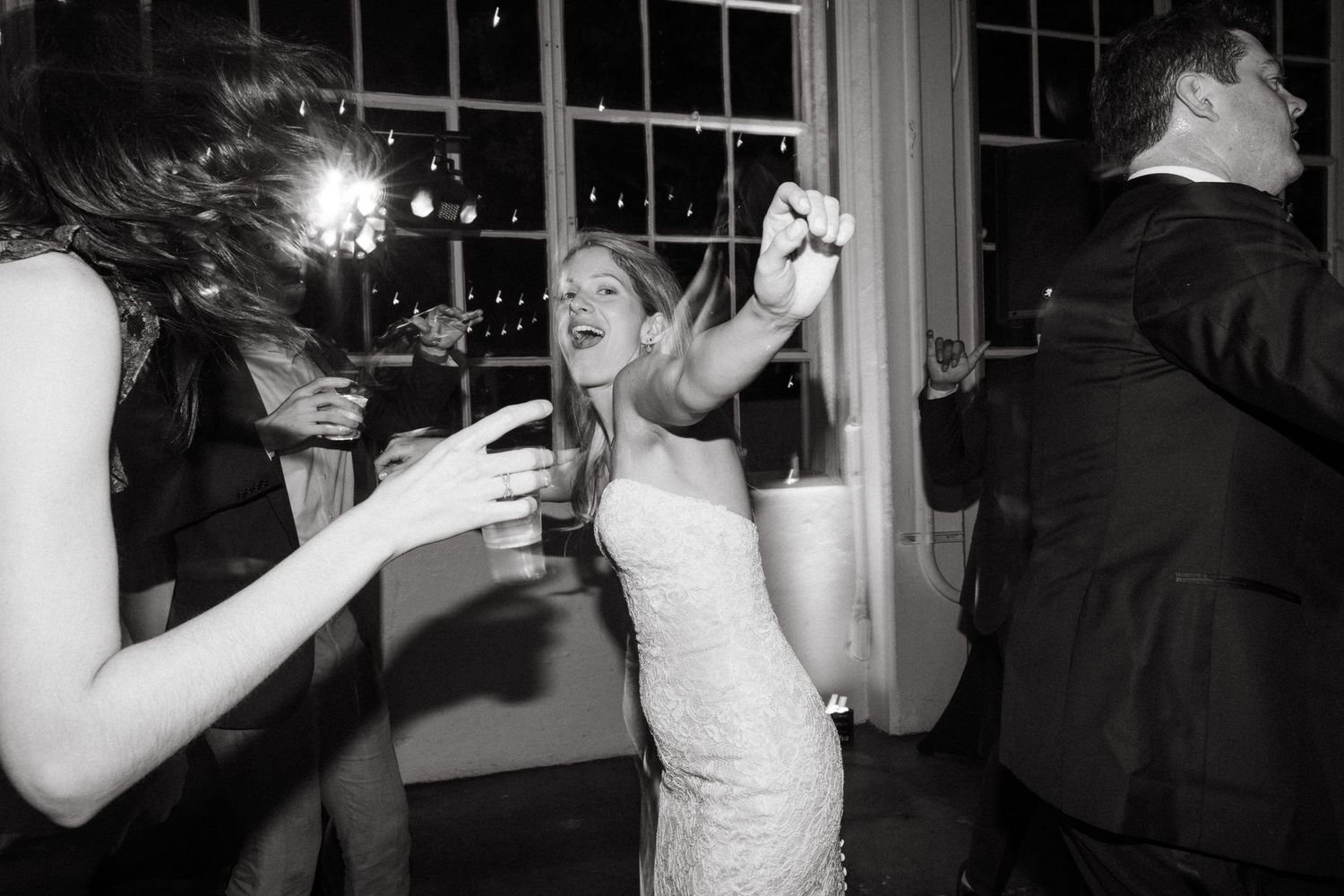 Wedding guests dance and celebrate with drinks at an evening reception.