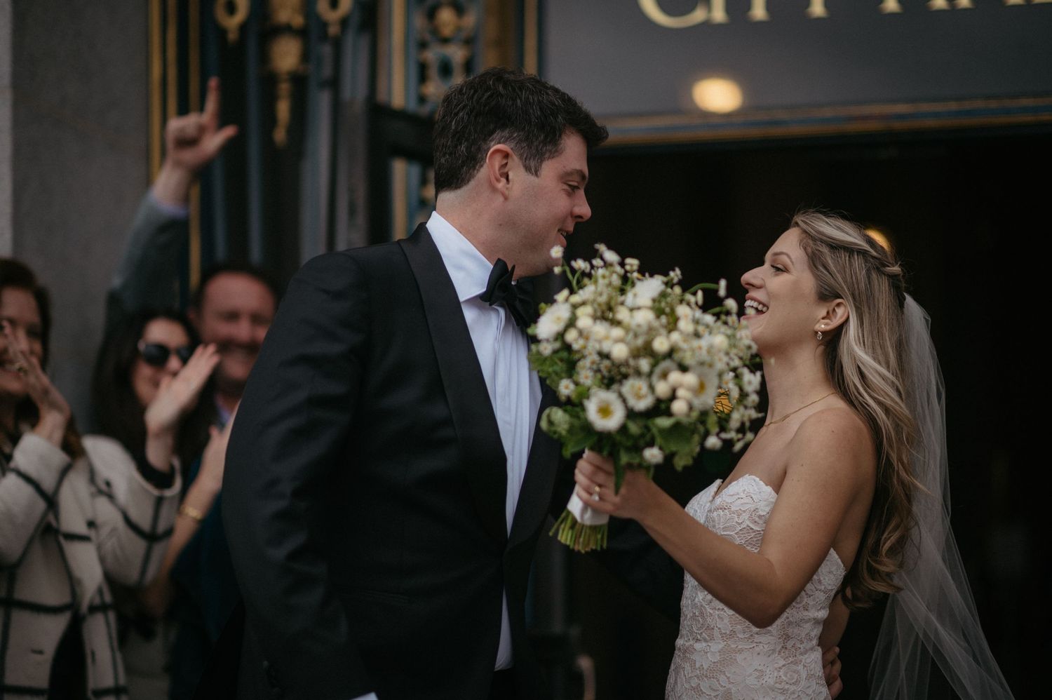 Candid moment of celebration outside City Hall's ornate entrance after wedding ceremony.