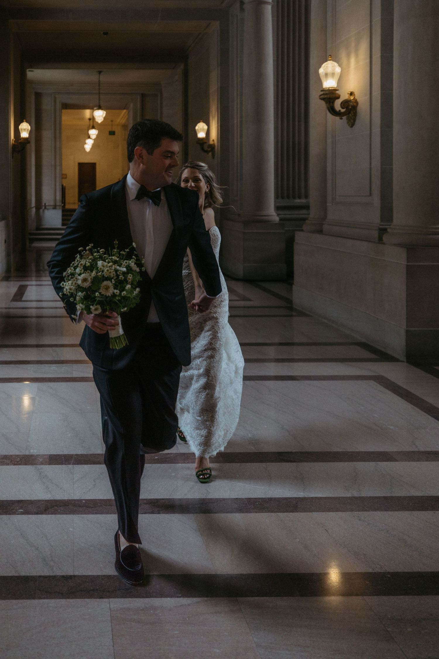 A couple strolls down a marble hallway with vintage lighting fixtures.