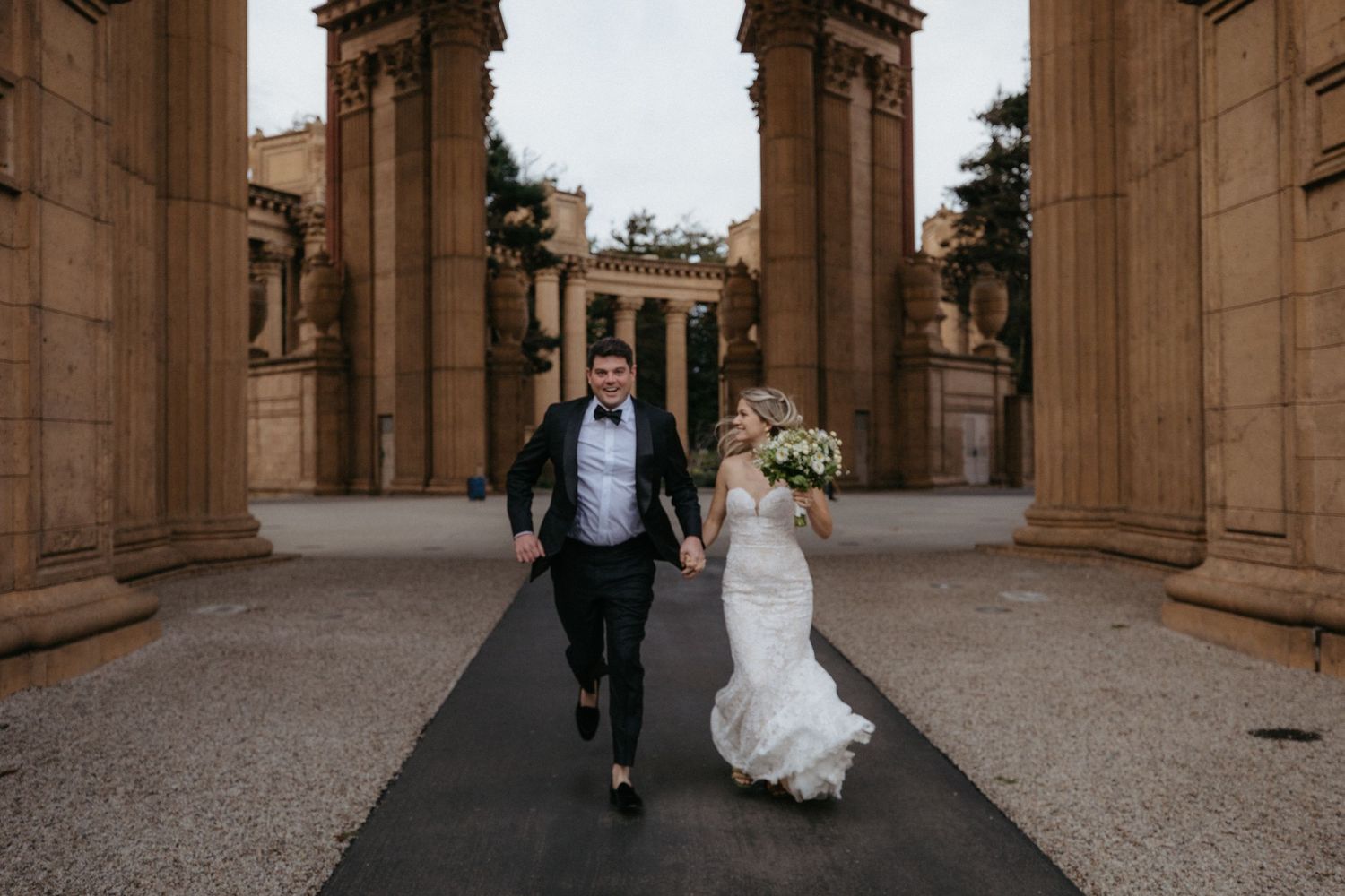 A wedding couple walks through majestic stone archways at a historic venue.
