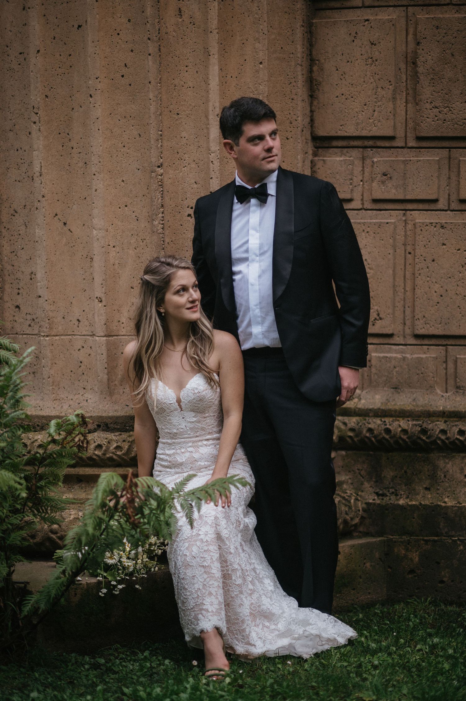 Elegant wedding portrait with couple posed against stone architecture.