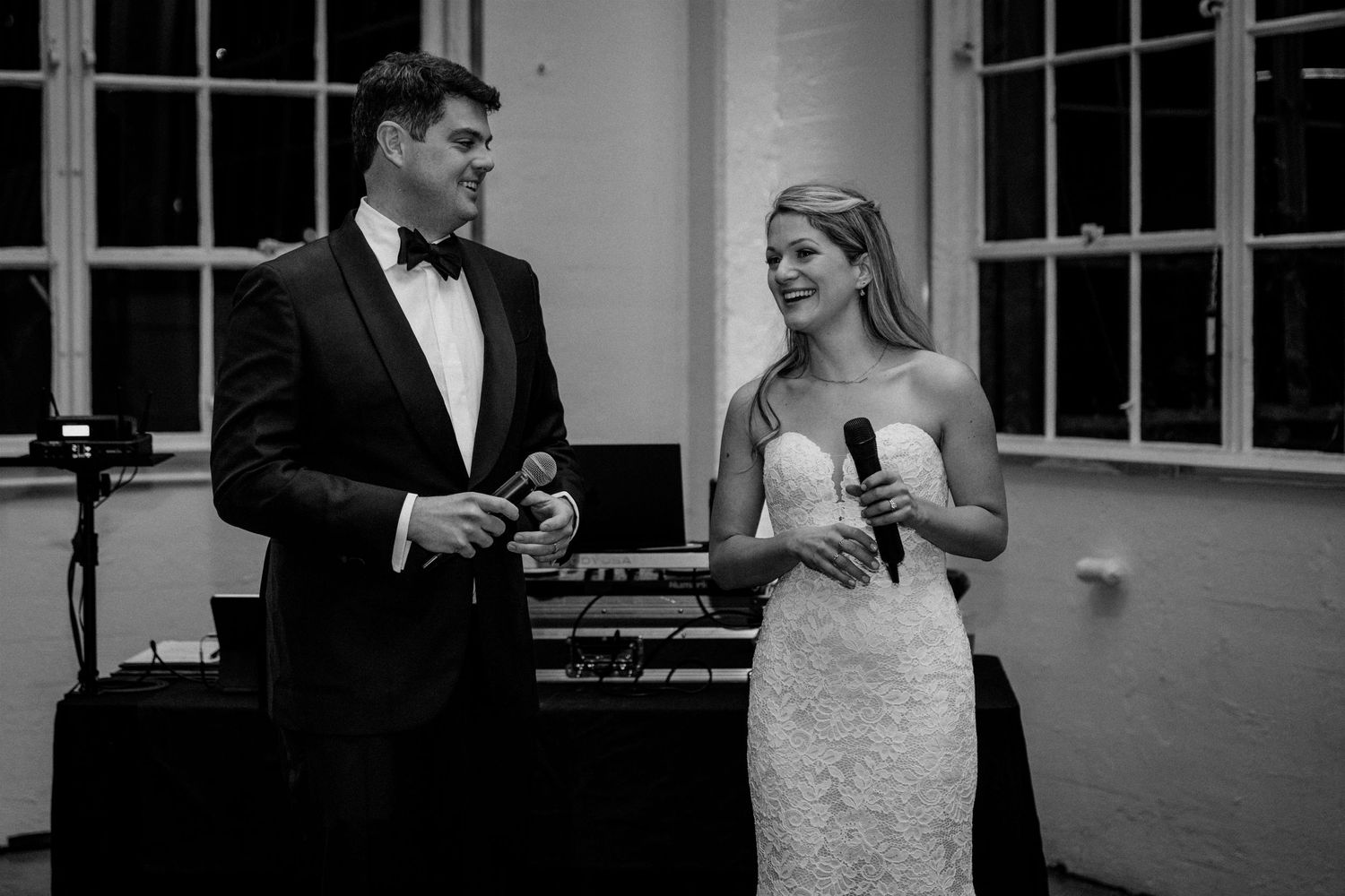 Black and white photo of newlyweds sharing a speech moment at their wedding reception.