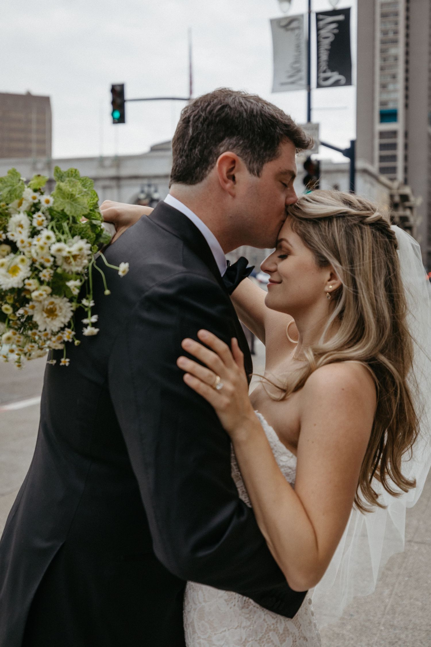 Intimate moment between newlyweds on city street with spring bouquet.