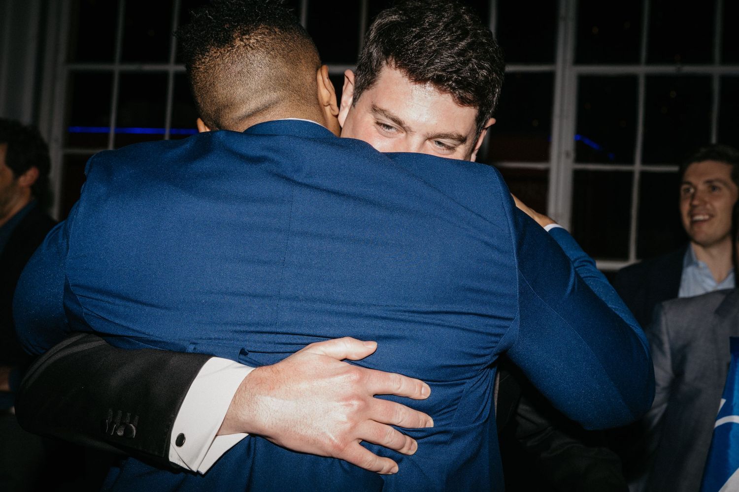 Two people in blue suits share an emotional embrace at a formal event.
