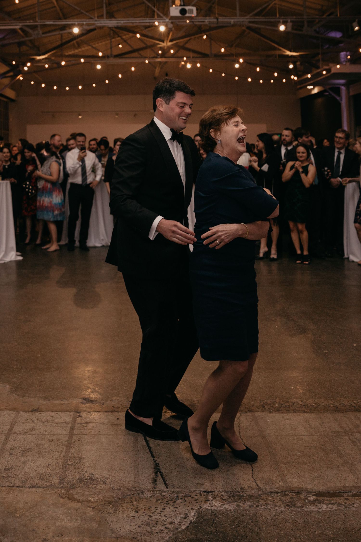 Wedding guests dance together on a rustic dance floor under string lights.