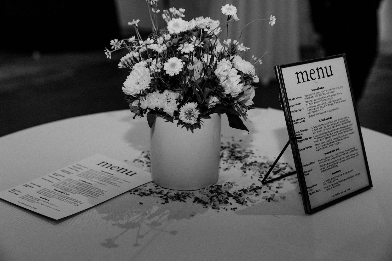 A black and white photo of wedding menus and floral centerpiece on a table.