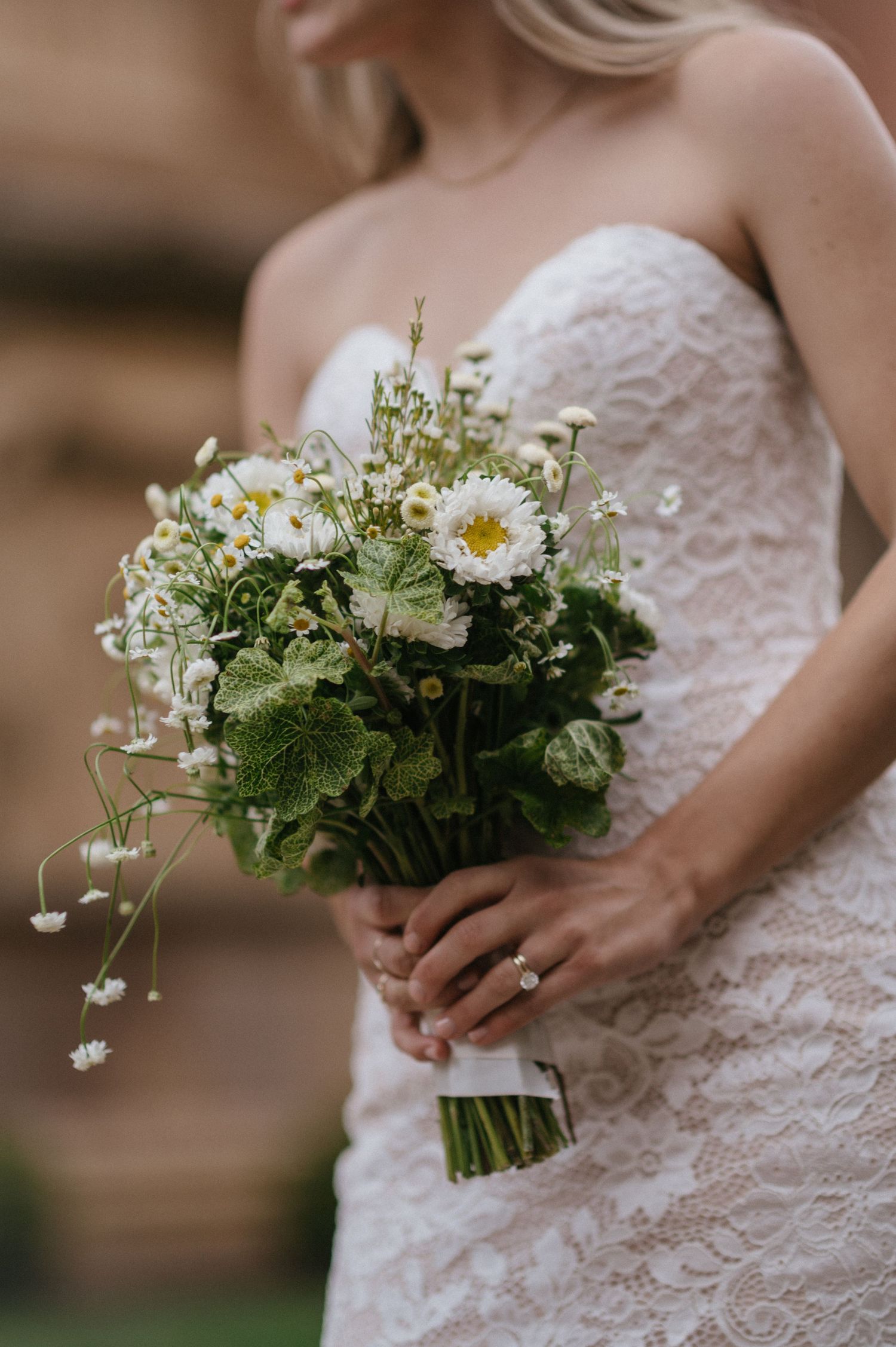 Delicate white and green wildflower wedding bouquet held against lace wedding dress.