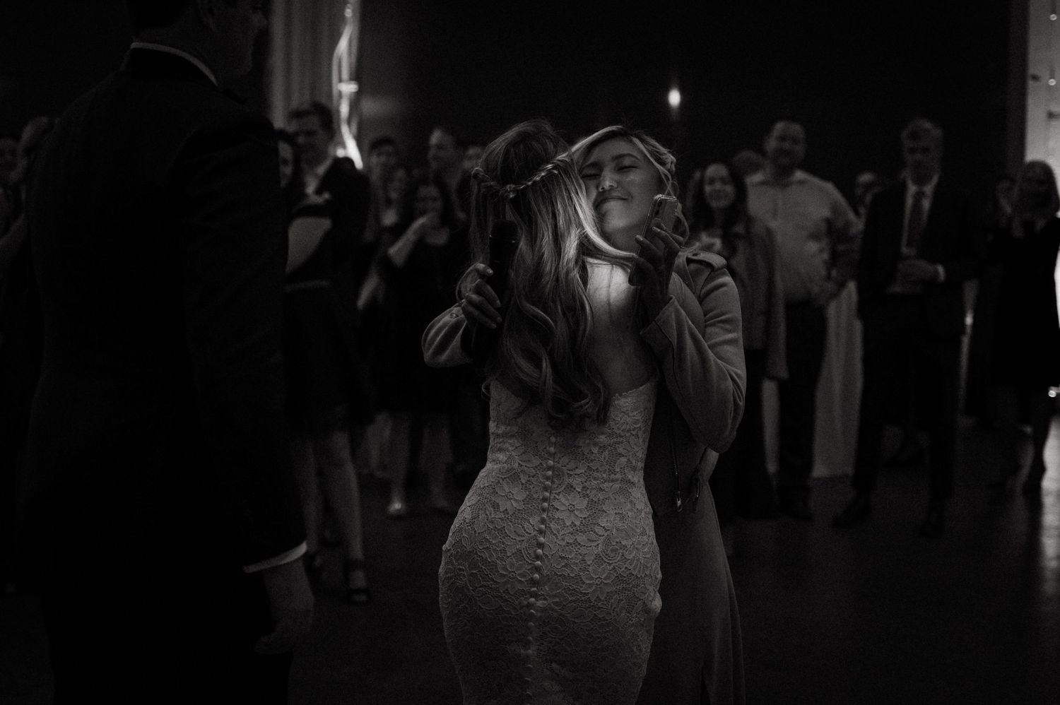 A bride in a fitted lace dress dances in dramatic lighting at her wedding reception.