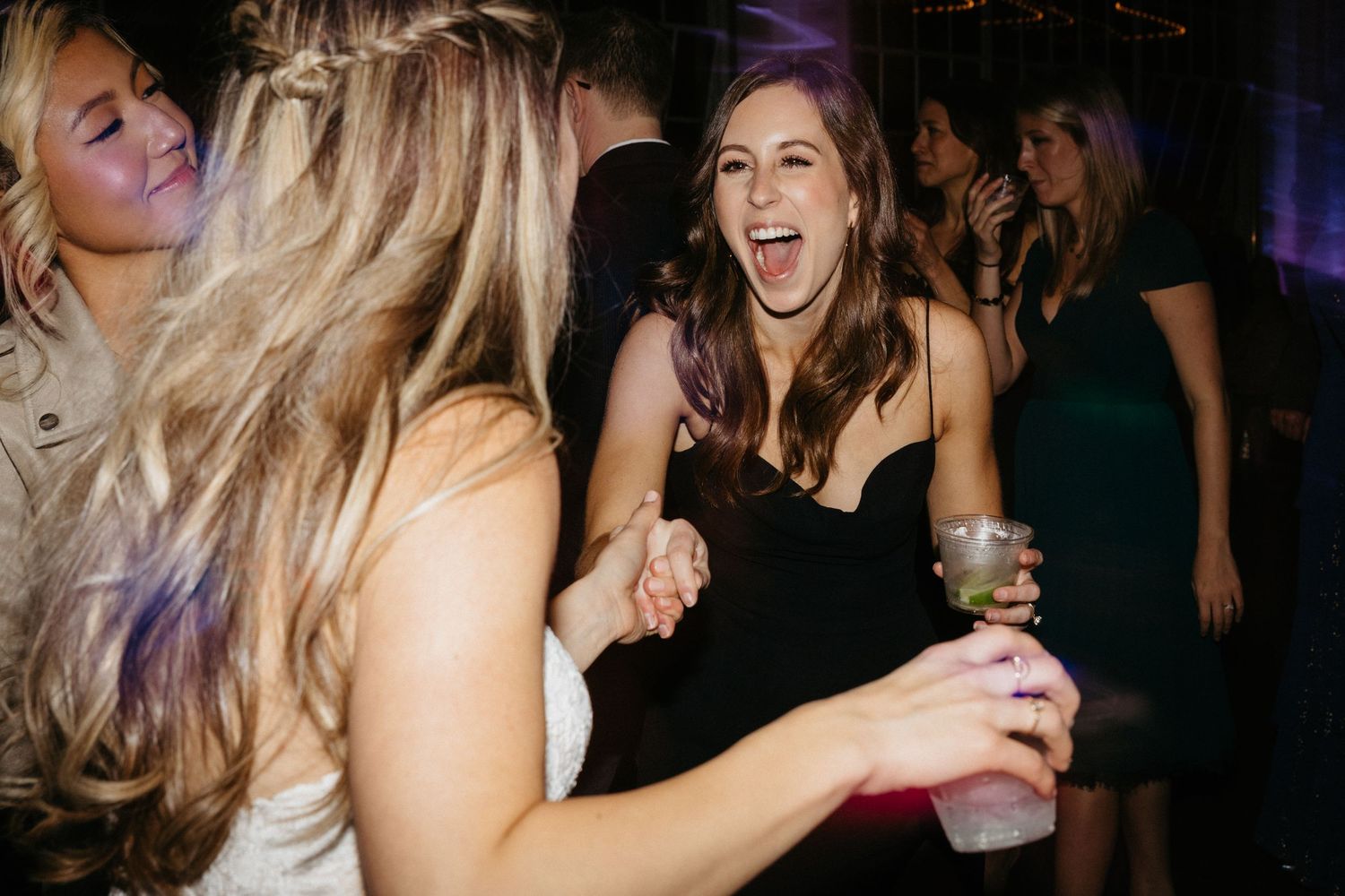 Party guests laugh and dance together on a dimly lit dance floor at a celebration event.