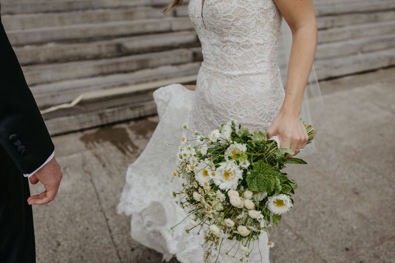 Close-up of white and green wedding bouquet with lace wedding dress detail.