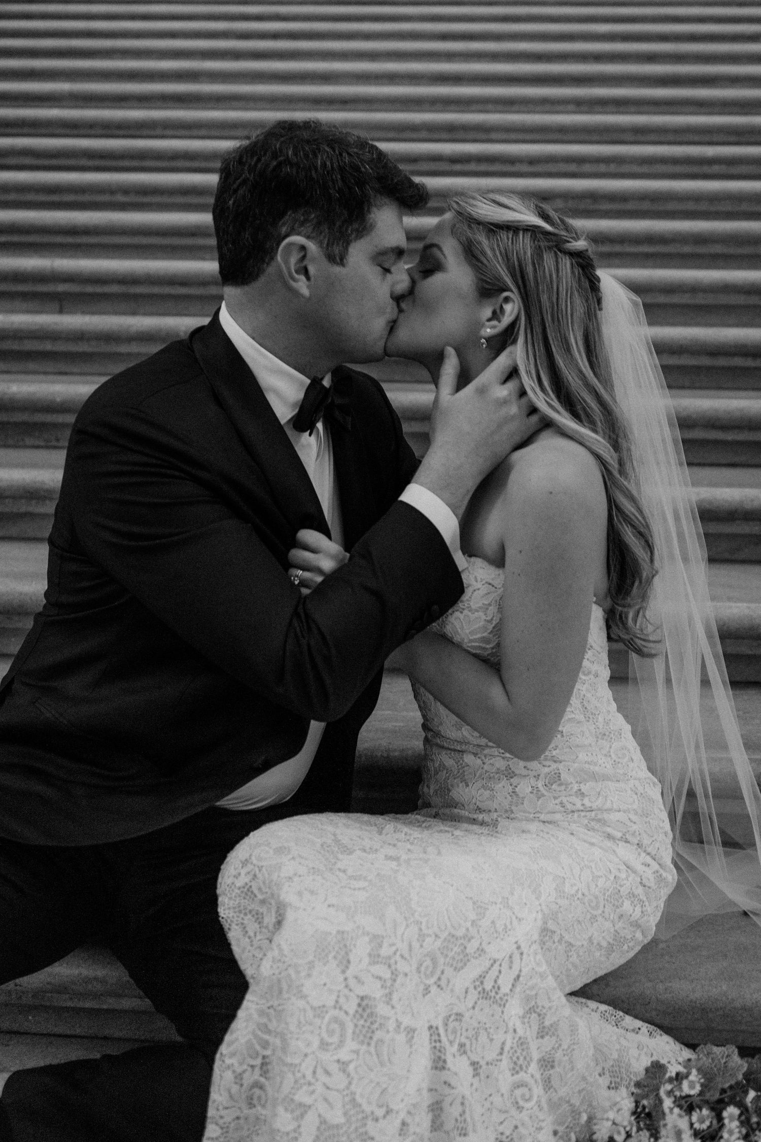 Close up of romantic moment on grand staircase with lace wedding gown and formal attire.