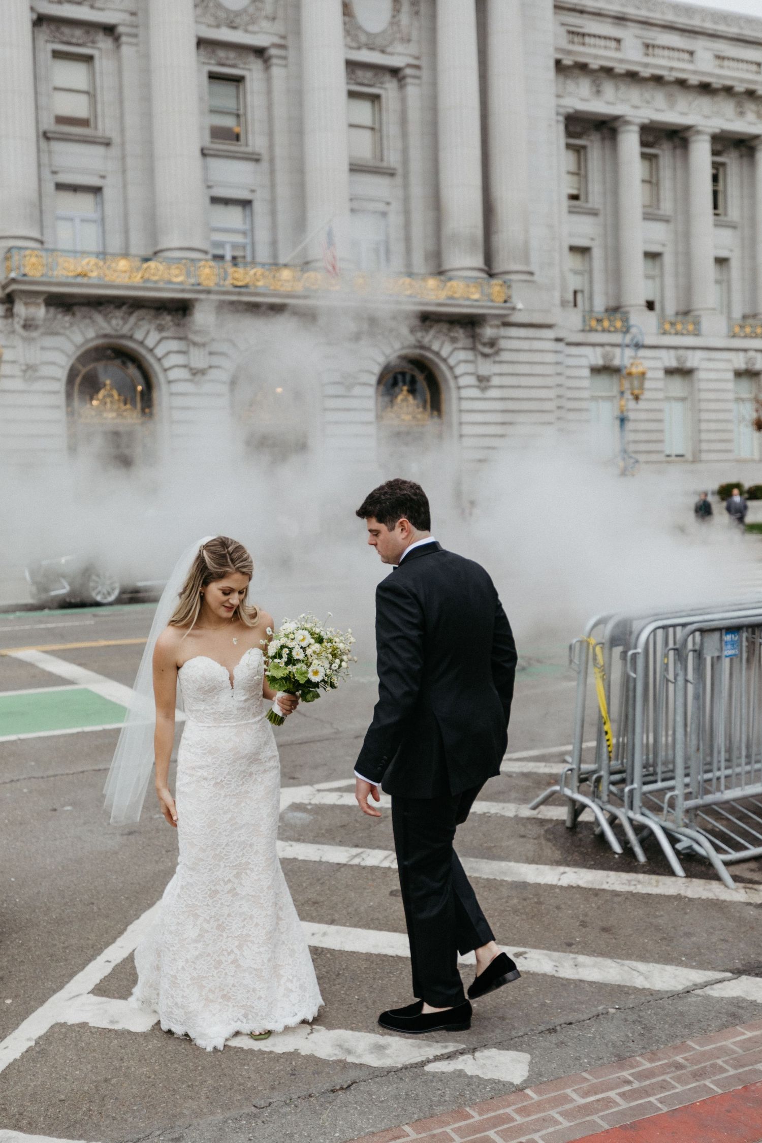 Couple walks through fog outside historic City Hall building after wedding ceremony.