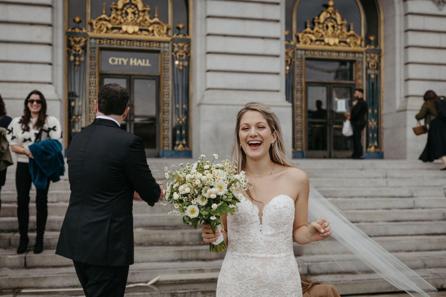 Newlyweds celebrate on City Hall steps with elegant bouquet and flowing veil.