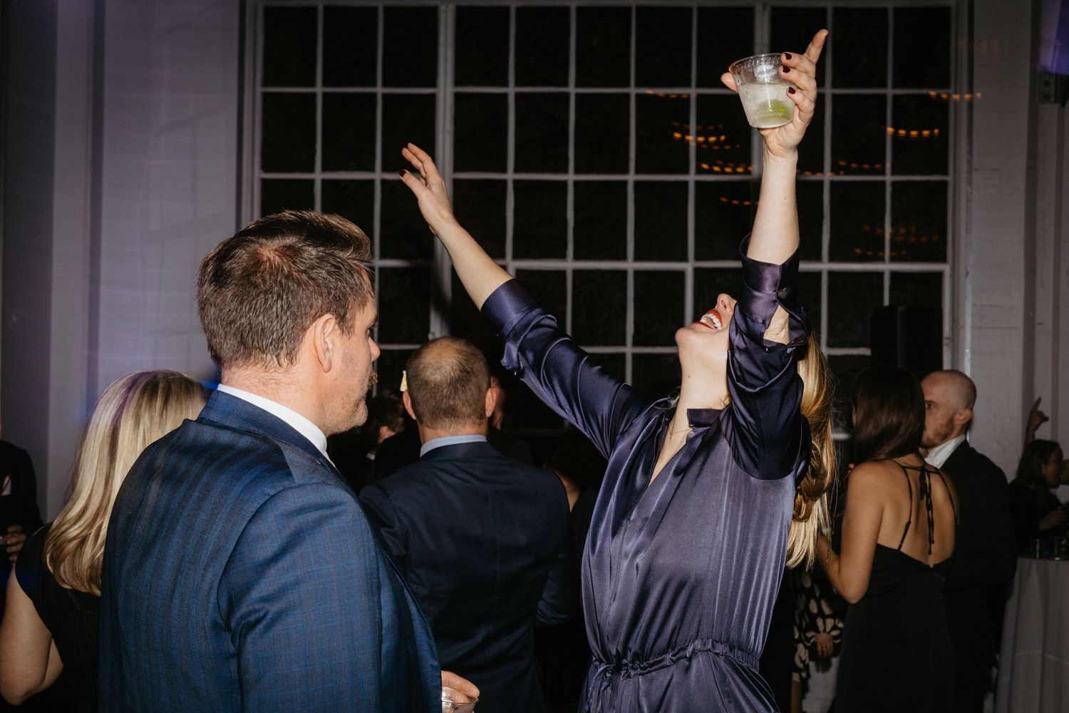Guests dancing with raised arms at an indoor evening celebration.