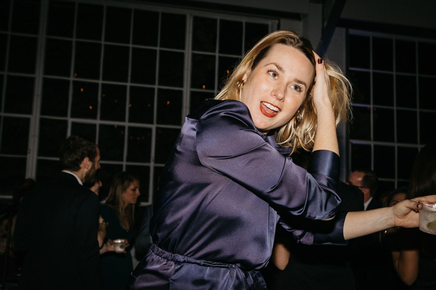 Person in purple satin top dancing enthusiastically at a nighttime event.