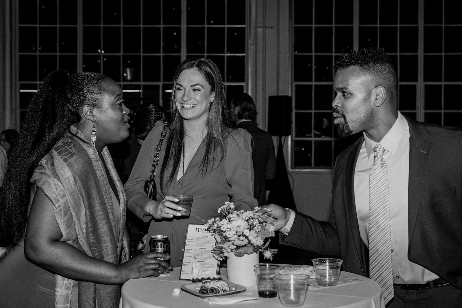 Wedding guests engage in conversation around a table with floral centerpieces.
