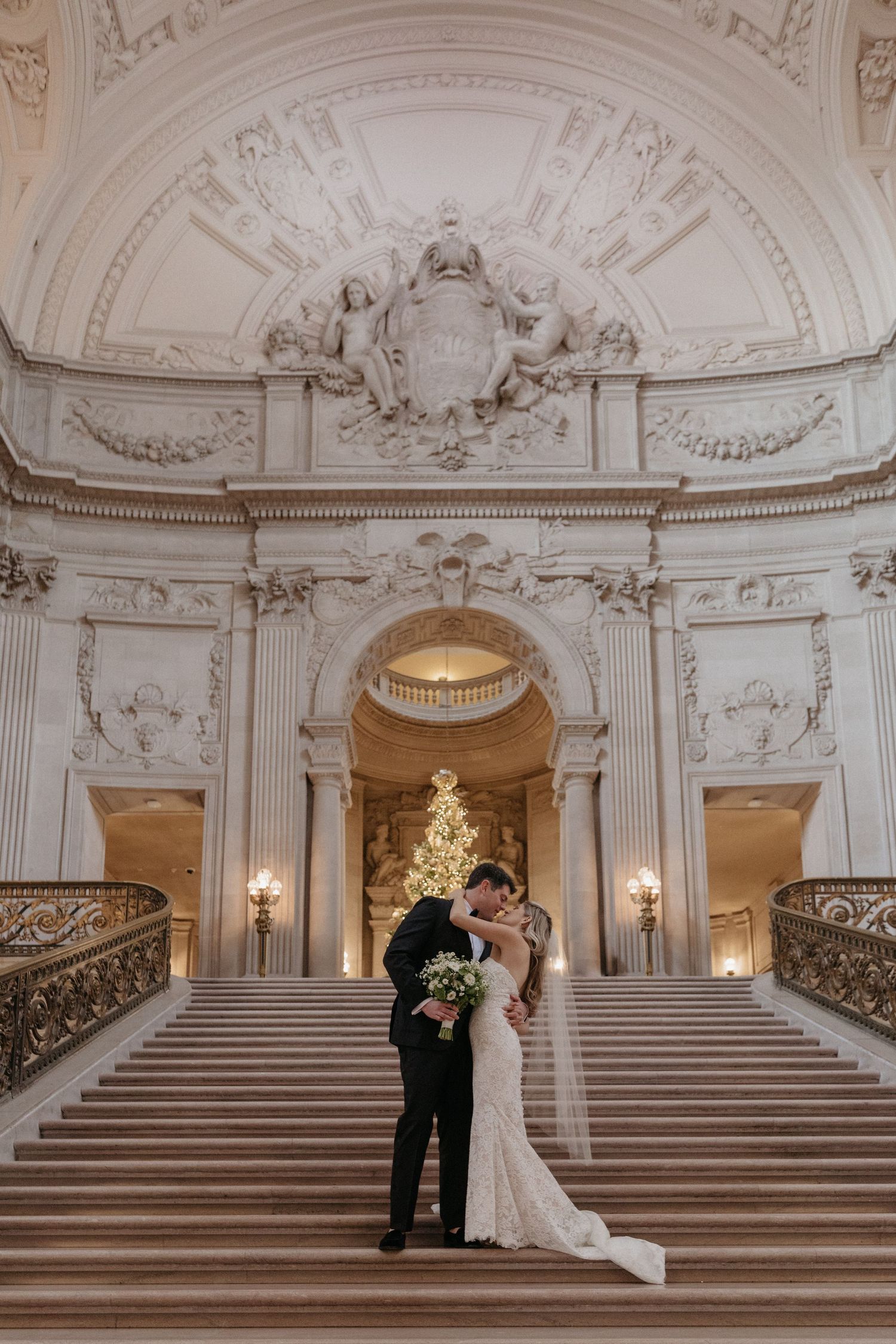 A stunning wedding portrait on grand marble stairs with ornate Beaux-Arts architectural details.