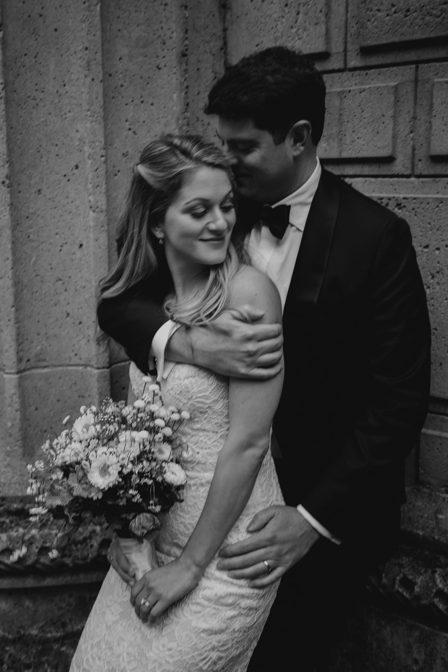 Intimate black and white wedding portrait against textured stone wall.