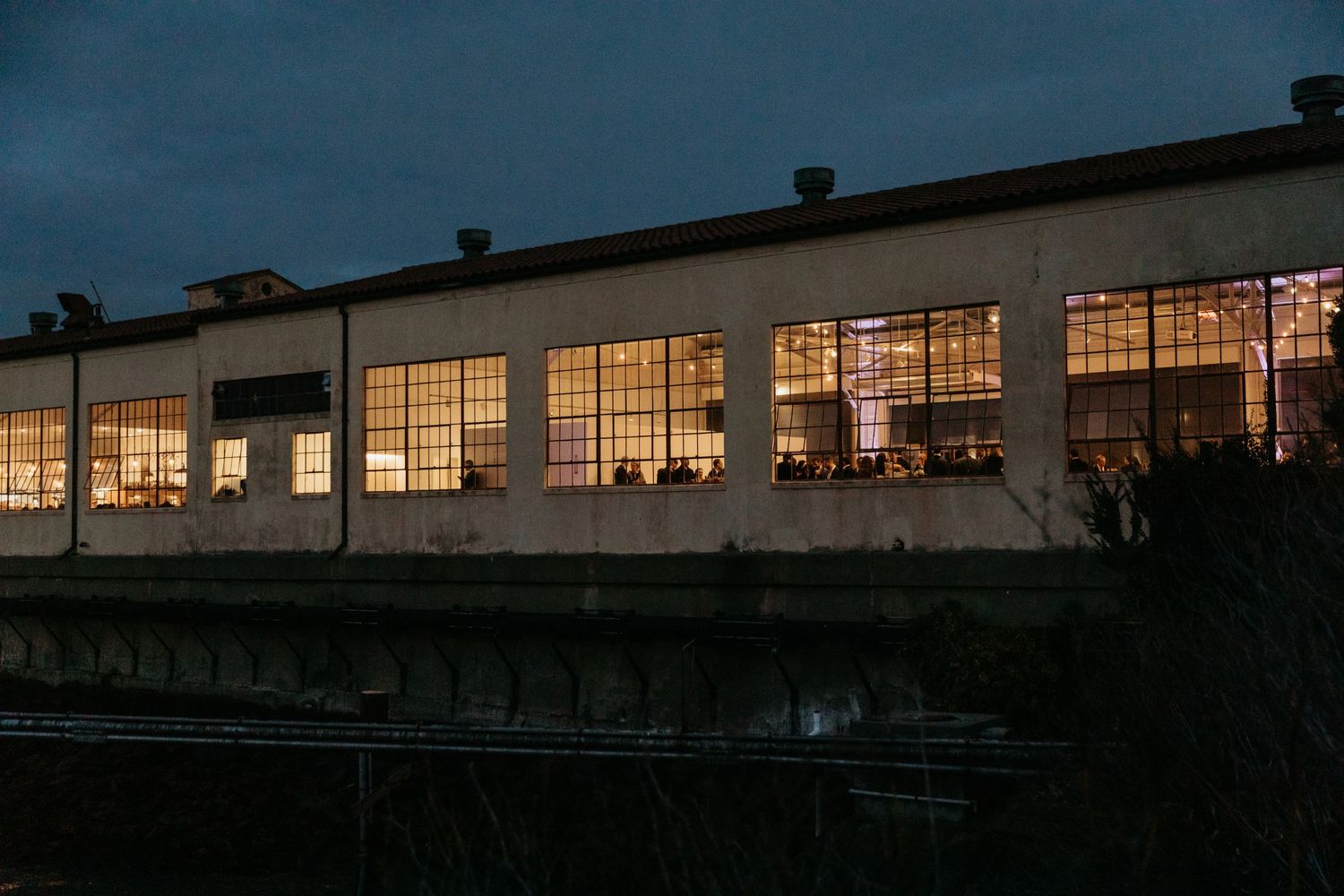 Industrial building with illuminated windows glowing at dusk creates a warm atmospheric scene.