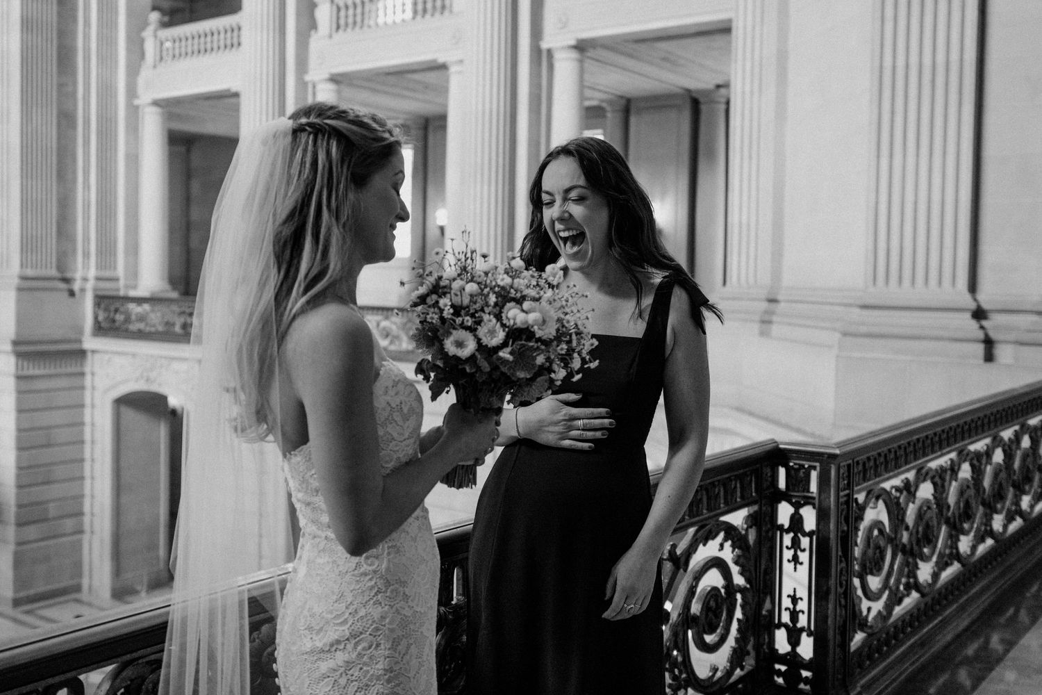Black and white photo of two people sharing flowers and smiles along an ornate balcony railing.