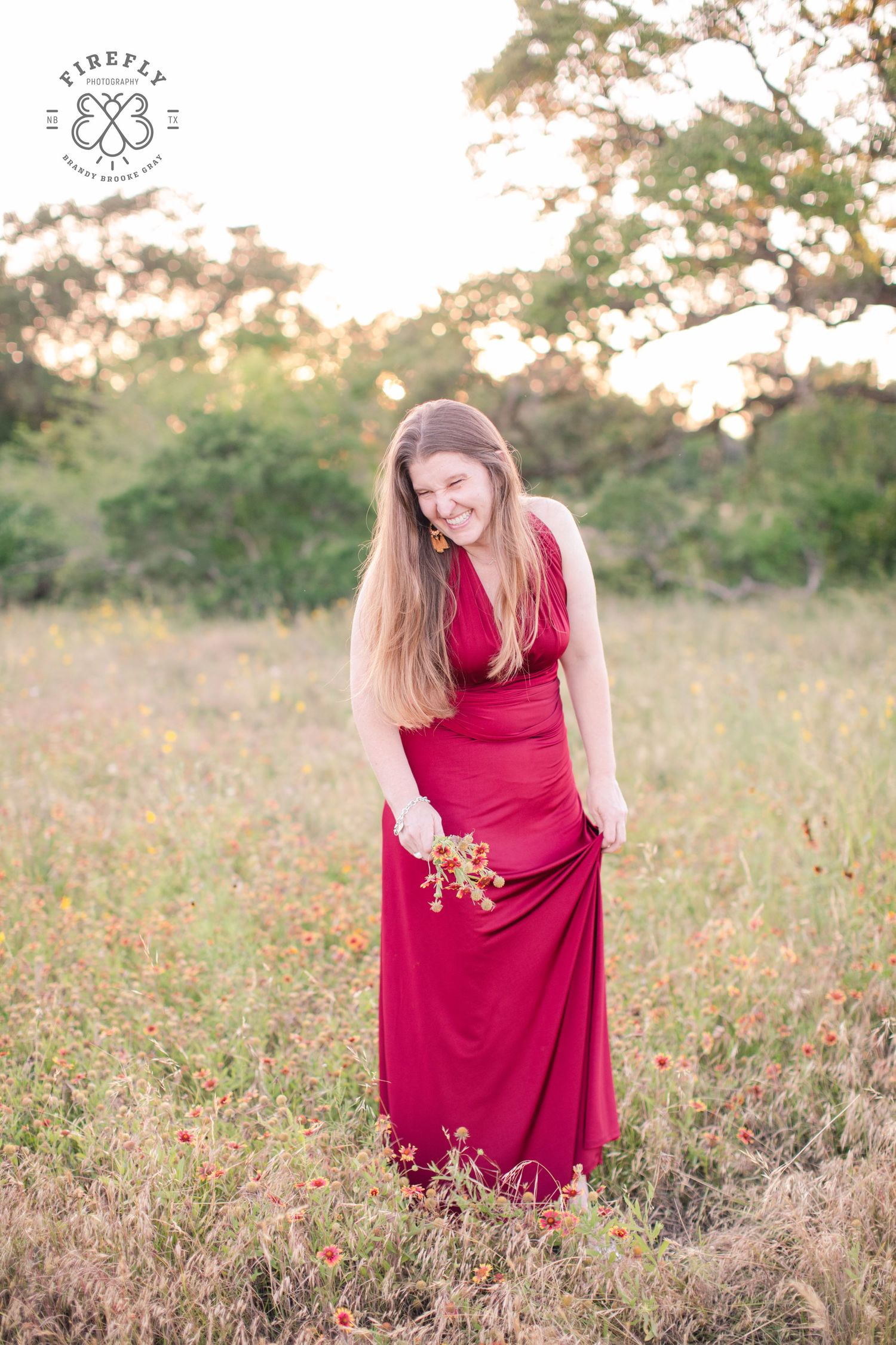 Woman in flowing red dress stands in golden wildflower field at sunset.
