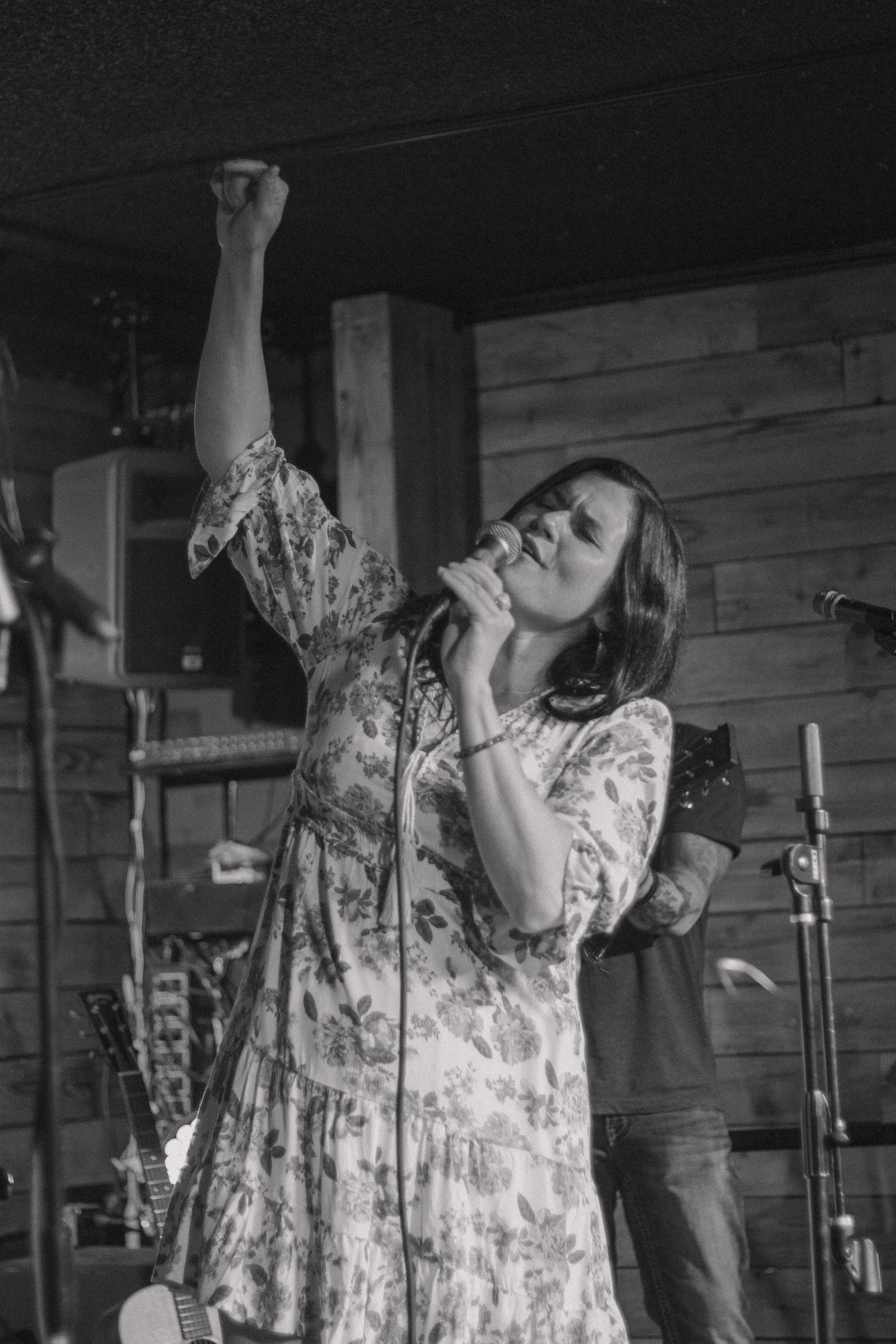 A performer on stage in a floral dress singing passionately during a live show.